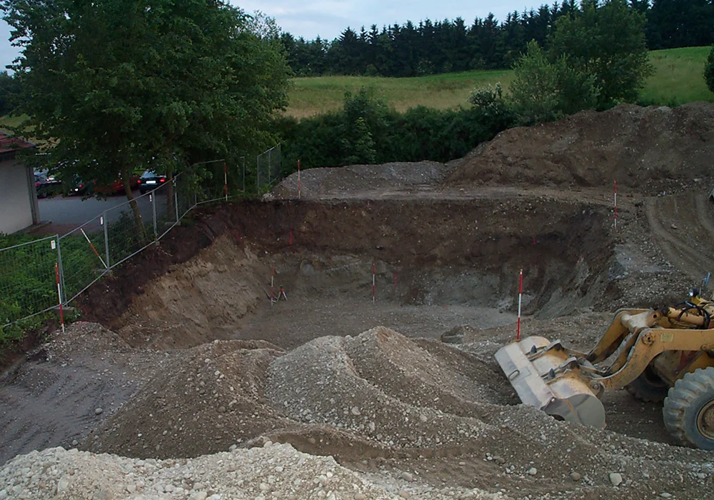 Große Baugrube mit Kies- und Schotterhaufen und Radlader bei Erdarbeiten für Tankanlage