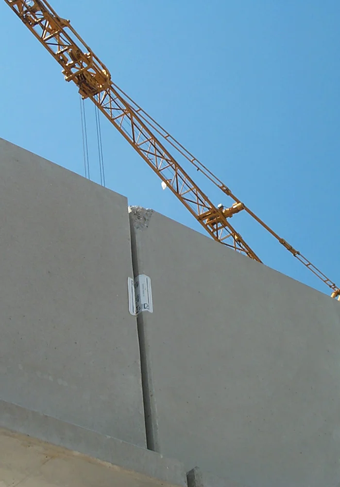 Baukran hebt Betonfertigteile über große Betonwand auf Baustelle