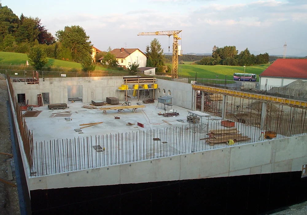 Rohbau eines Gewerbegebäudes mit Betonwänden, Bewehrung und Baukran im Hintergrund