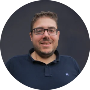 Maximilian Pauker mit Brille und kurzem Bart lächelt in die Kamera, trägt dunkelblaues Polohemd vor neutralem Hintergrund.