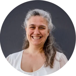 Lächelnde Renate Ganslmaier mit grauen, lockigen Haaren vor dunklem Hintergrund, trägt eine weiße Bluse.