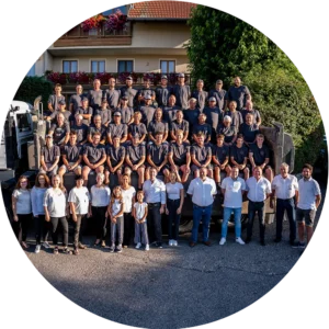 pauker-bau-gmbh-direktkontakt-team Gruppenfoto eines großen Bauunternehmens-Teams mit über 50 Personen, teils in Arbeitskleidung, aufgenommen im Freien vor einem LKW.