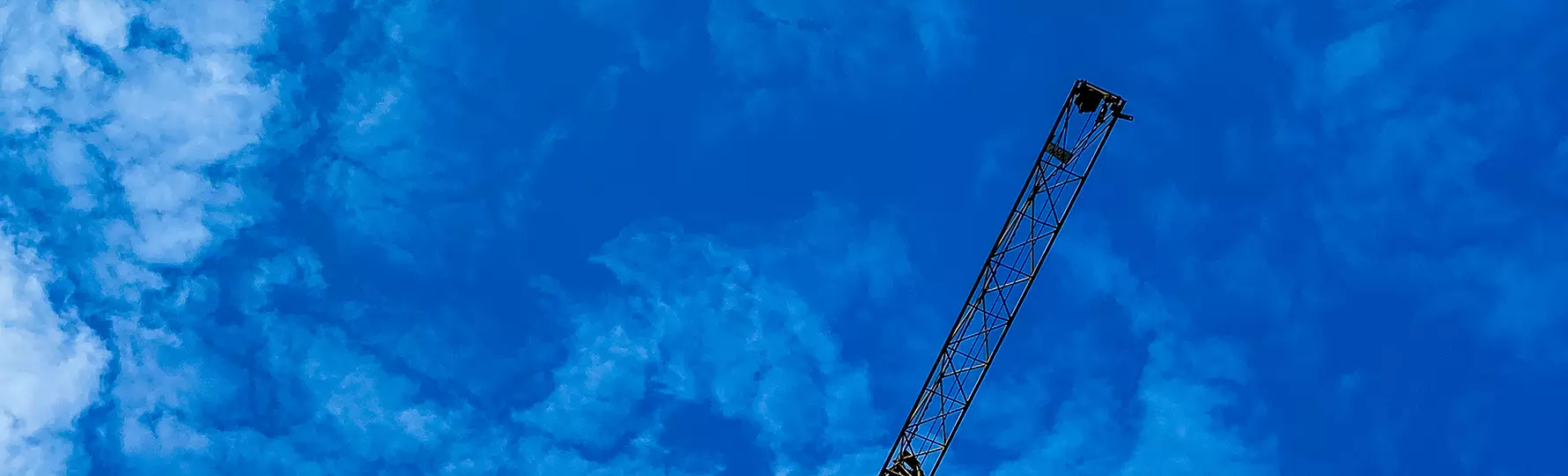 Spitze eines Baukrans ragt schräg in den blauen Himmel mit vereinzelten Wolken.