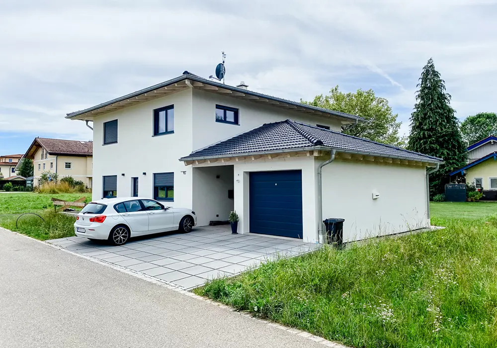 Modernes Einfamilienhaus mit Garage, blauen Fensterläden und weißem Auto in der Einfahrt.