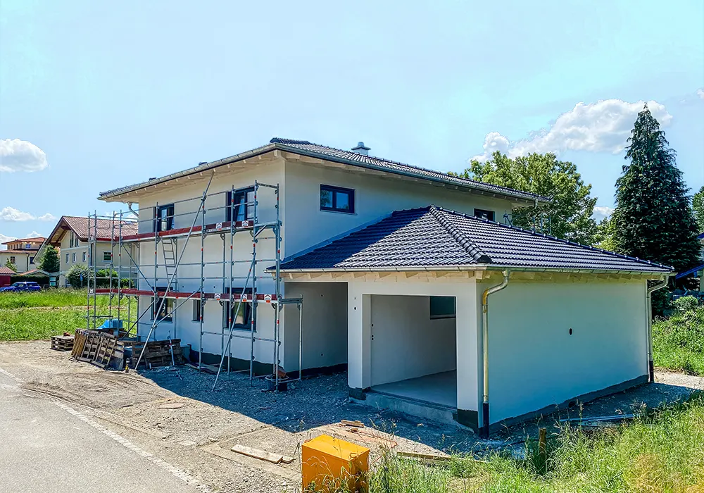 Zweistöckiges Neubauhaus mit angebauter Garage und Baugerüst an der Fassade, umgeben von Wiese.