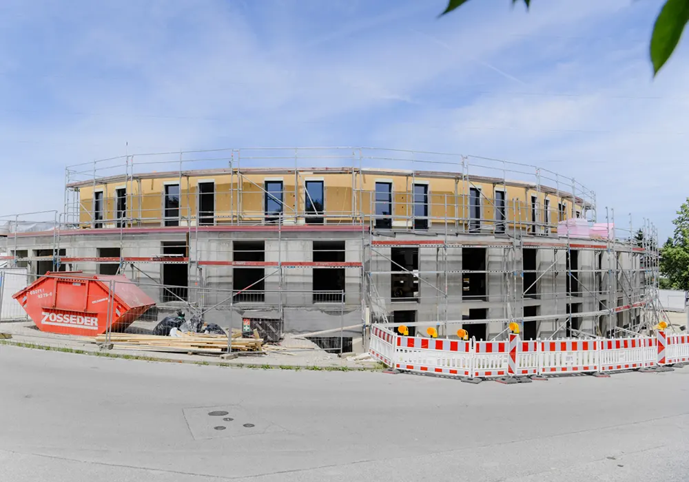 Zweistöckiges Gebäude im Rohbau mit Gerüst, gelber Container und Strommast im Hintergrund.