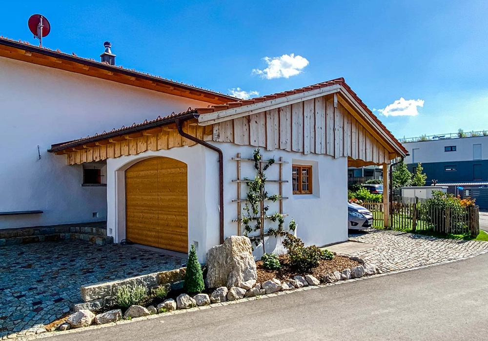 Einfahrt mit Steinpflaster vor Garage mit Holztor an einem Haus mit Garten und Spalierpflanze.