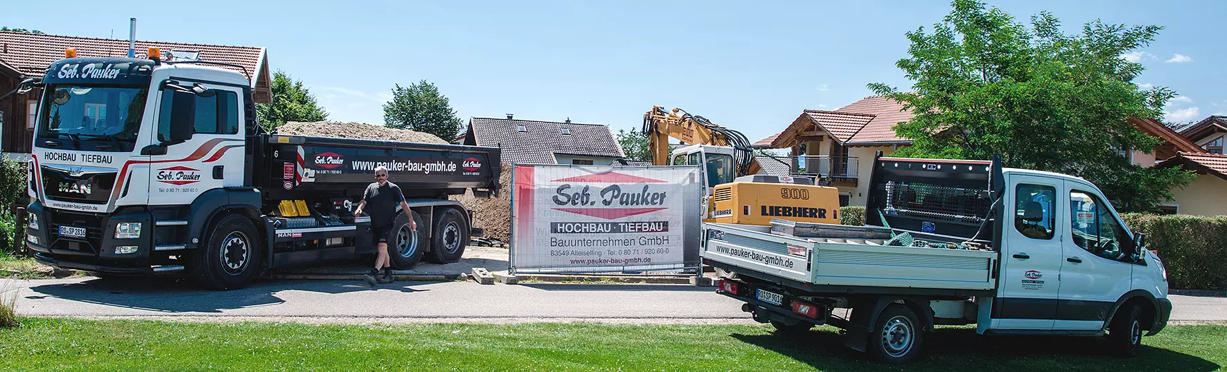 Bauunternehmen-Fahrzeuge und Bagger vor Bauzaun mit Banner von Seb. Pauker Hochbau Tiefbau GmbH.