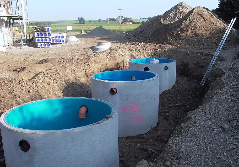 Drei große Beton-Schächte mit blauer Innenverkleidung und Rohranschlüssen werden in einer Baugrube installiert.