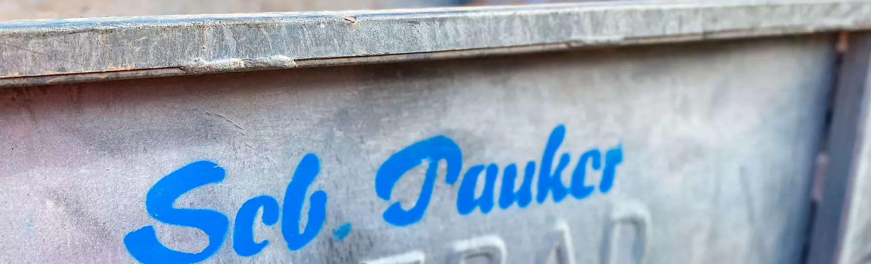 Detailaufnahme eines Metallcontainers mit blauer Aufschrift ‚Seb. Pauker‘.