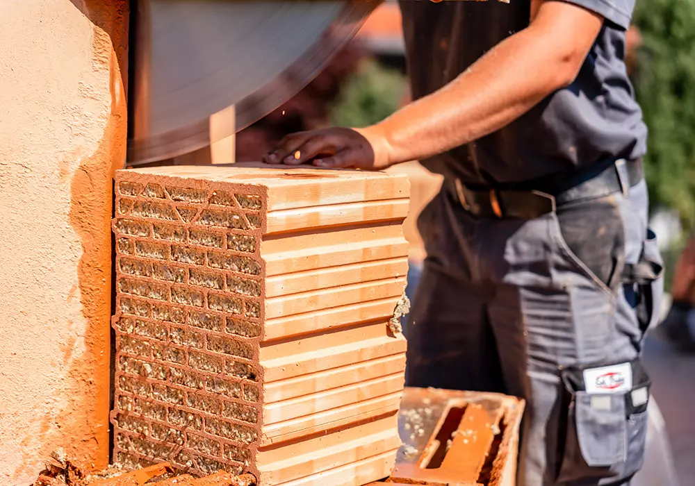 Bauarbeiter schneidet roten Ziegelstein mit großer Kreissäge auf der Baustelle.