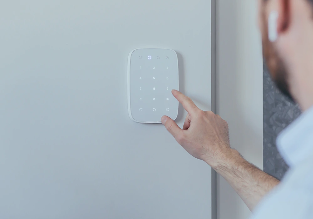 Person tippt auf ein beleuchtetes Wand-Bedienfeld mit Ziffern, vermutlich Teil einer Smart-Home- oder Alarmanlage.