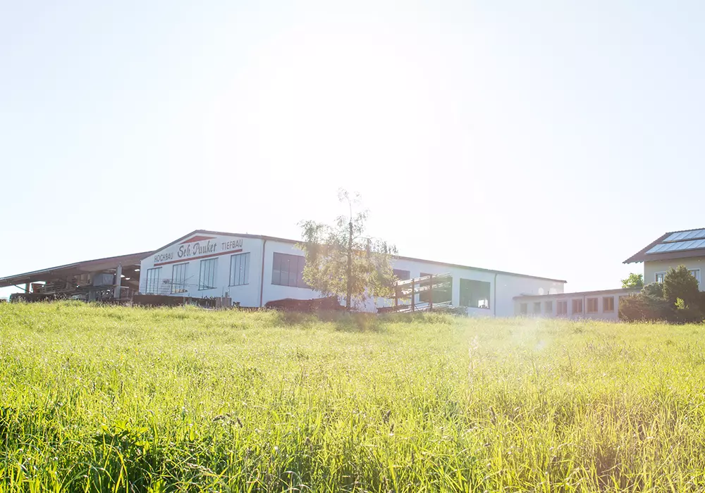 Firmengebäude von „Seb. Pauker Hochbau Tiefbau“ und benachbartes Wohnhaus mit Solaranlage auf einem sonnigen Wiesengrundstück.