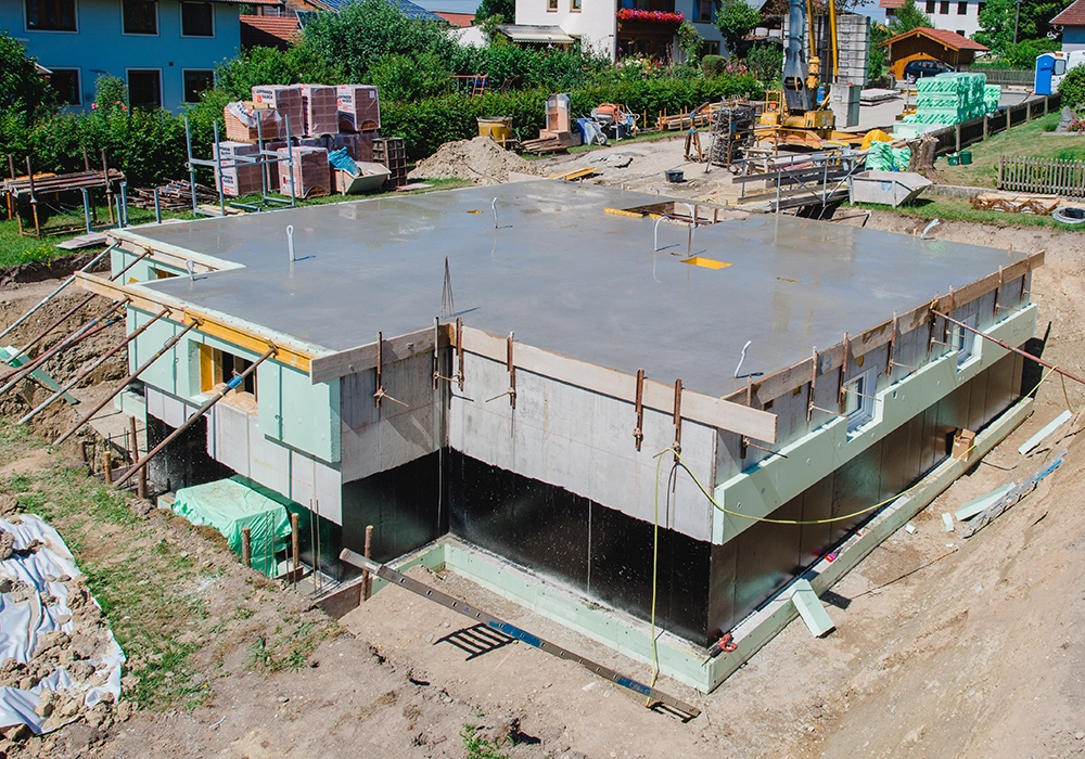 Kellerrohbau eines Einfamilienhauses mit frischer Betondecke auf einer aktiven Baustelle.