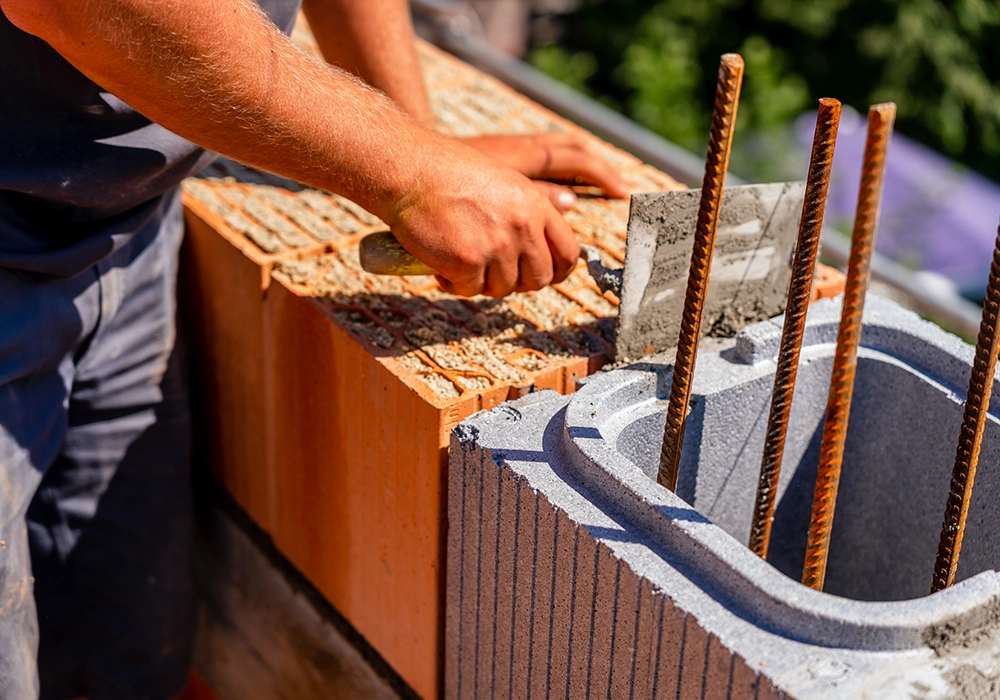 Mauerer trägt Mörtel auf Ziegel und Schalstein mit Bewehrungseisen auf.