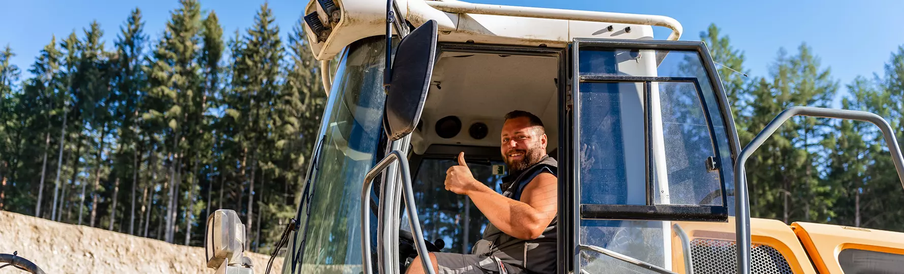 Lächelnder Bauarbeiter zeigt Daumen hoch in der Fahrerkabine einer Baumaschine.