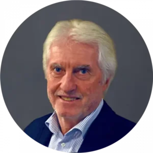 Porträt eines älteren Mannes mit weißem Haar, Anzug und Hemd, vor neutralem grauen Hintergrund.