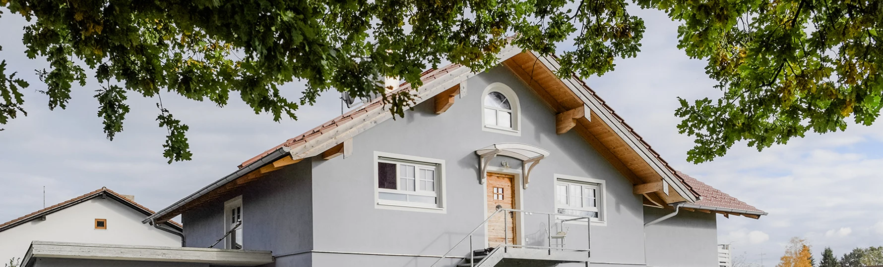 Modernisiertes Wohnhaus in Griesstätt mit Aufstockung, Außentreppe und Balkon unter großen Bäumen