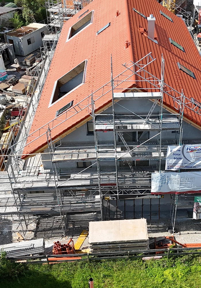 Rohbau eines Mehrfamilienhauses mit neu gedecktem Ziegeldach und Baugerüst