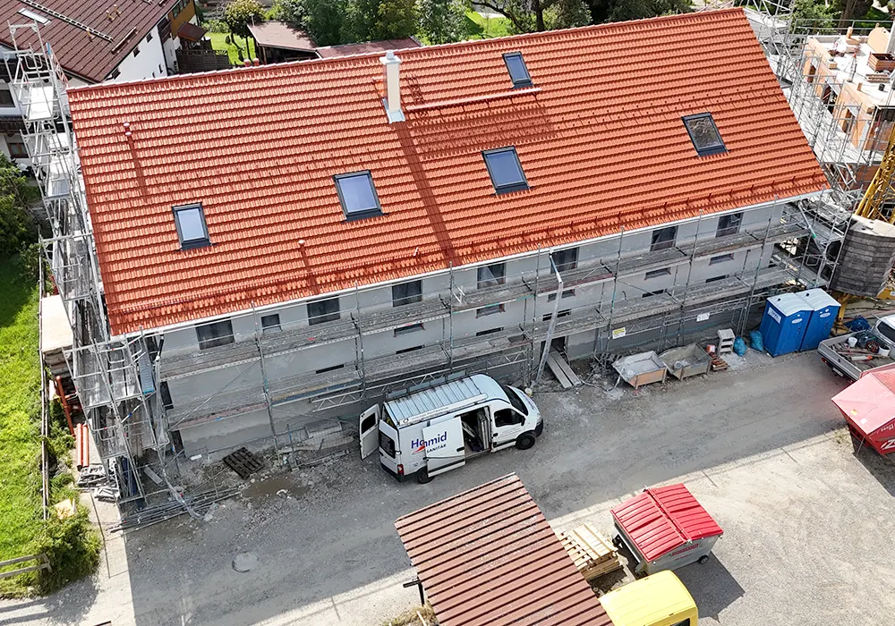 Mehrfamilienhaus im Rohbau mit Ziegeldach, Gerüst und Baustellenfahrzeug