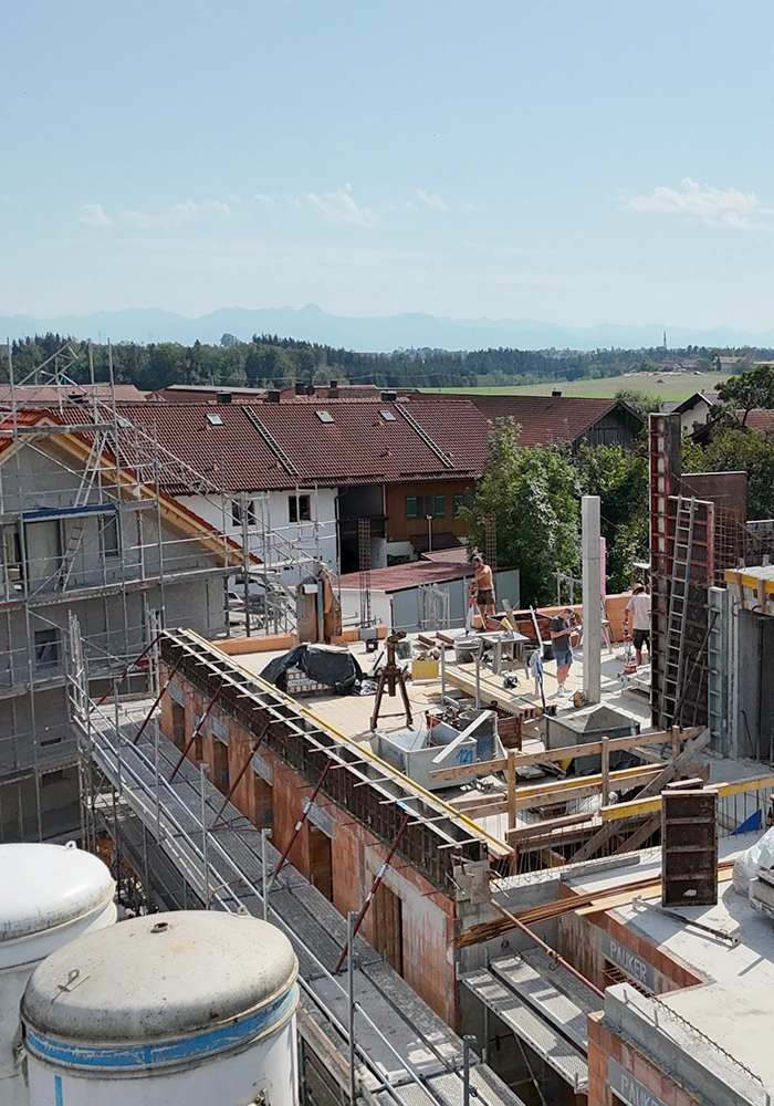 Baustelle mit Rohbau eines Mehrfamilienhauses und Bauarbeitern auf der Geschossdecke