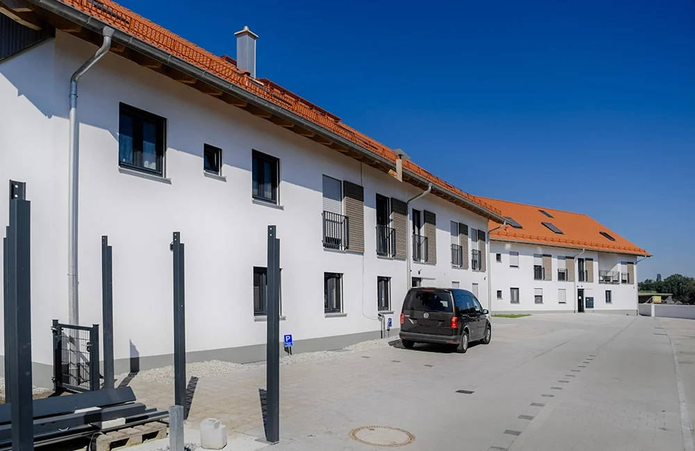 Mehrfamilienhaus mit weißer Fassade und rotem Ziegeldach in ländlicher Umgebung