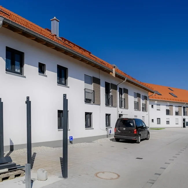 Mehrfamilienhaus mit weißer Fassade und rotem Ziegeldach in ländlicher Umgebung