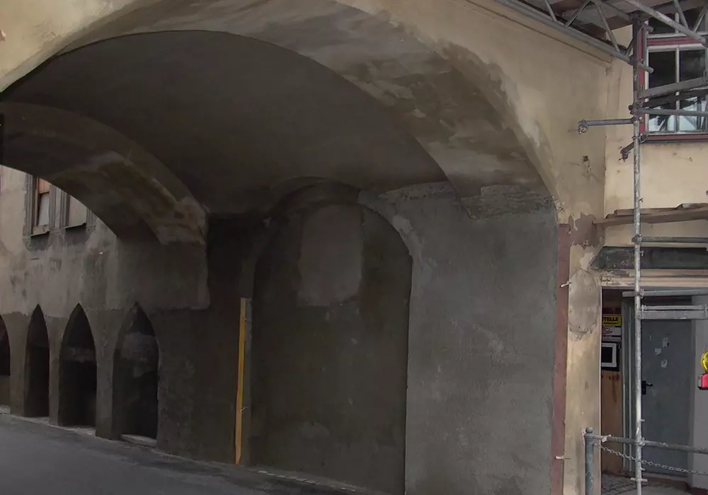 Brucktor mit Spitzbögen, teils frisch verputzt, daneben Baugerüst und Eingangstür.