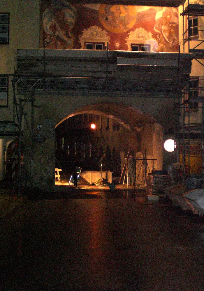 Nachts beleuchtetes Brucktor mit Gerüst und Wandgemälde, umgeben von Bauarbeiten und Materialien.