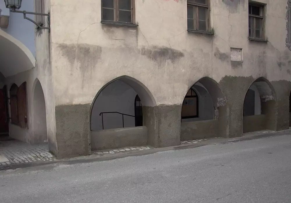 Altbau mit drei Spitzbögen über Bürgersteig, teils abblätternder Putz und sichtbare Fenster im oberen Stockwerk.