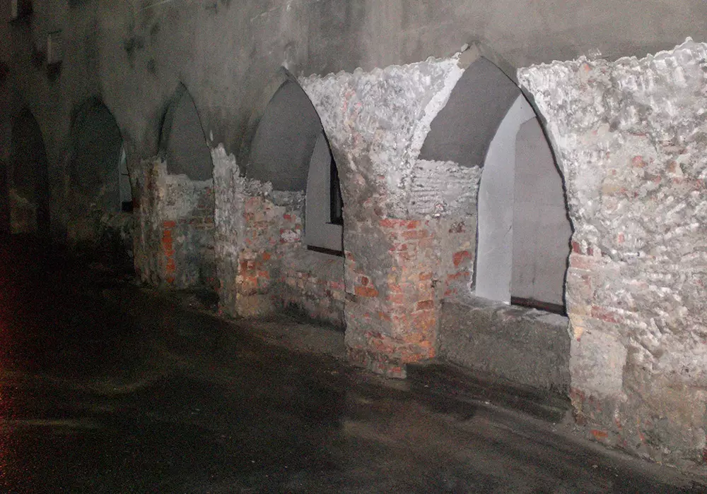 Alte gemauerte Bögen mit sichtbaren Ziegeln und abgeplatztem Putz entlang einer dunklen Hauswand bei Nacht.