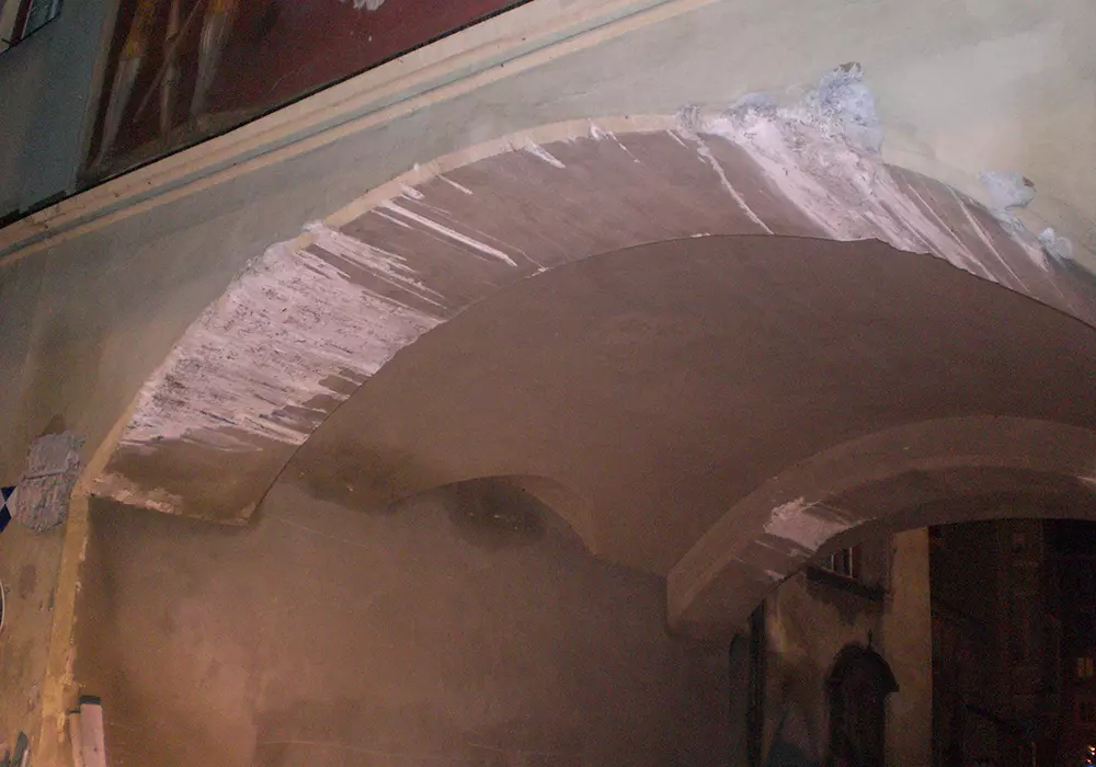 Nahaufnahme eines alten Gewölbebogens mit abgeplatztem Putz an Decke und Wand in dunkler Umgebung.