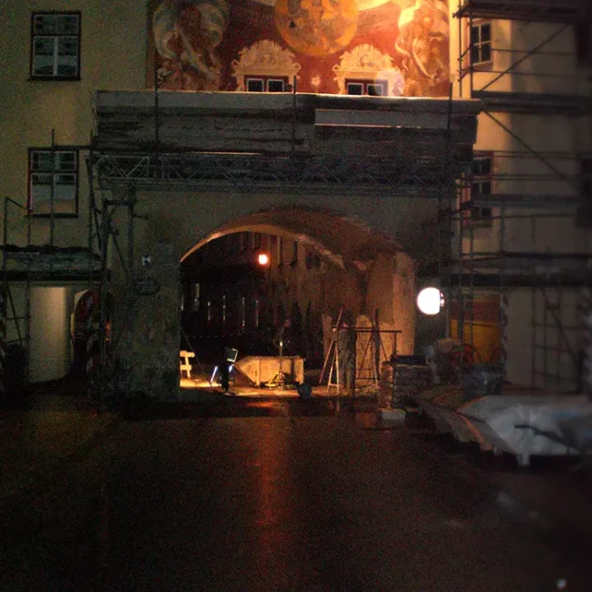 Nachts beleuchteter Torbogen mit Gerüst und Wandgemälde, umgeben von Bauarbeiten und Materialien.