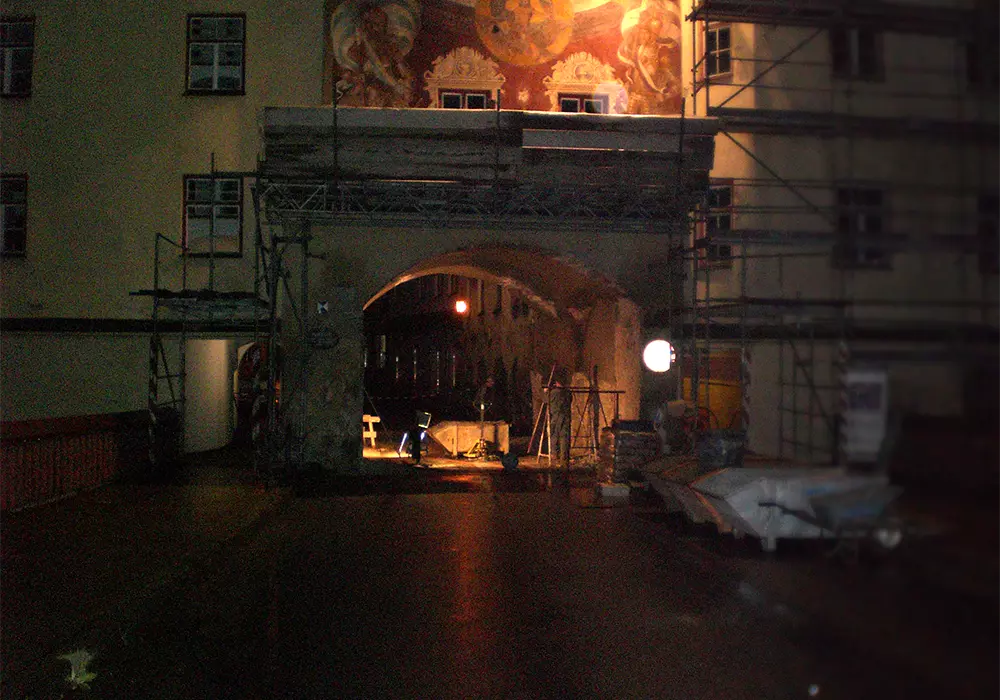 Nachts beleuchteter Torbogen mit Gerüst und Wandgemälde, umgeben von Bauarbeiten und Materialien.