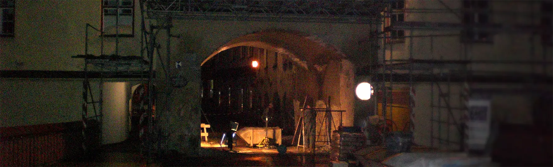 Nachts beleuchteter Torbogen mit Gerüst und Wandgemälde, umgeben von Bauarbeiten und Materialien.