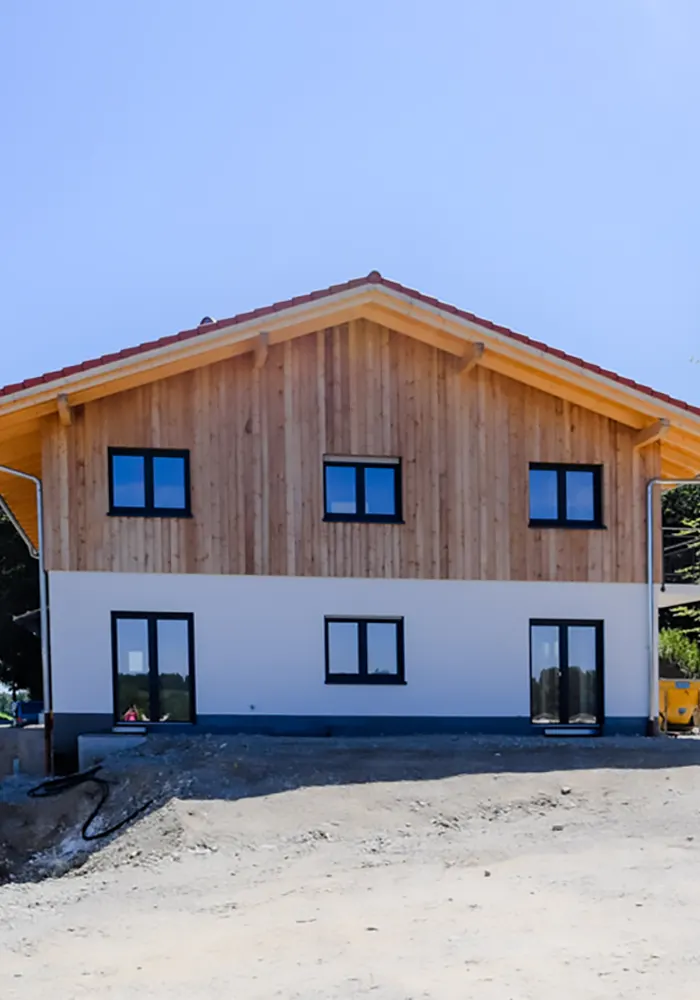 Neubau mit Satteldach, Holzfassade oben und weißen Wänden unten, fotografiert frontal auf Baustelle.