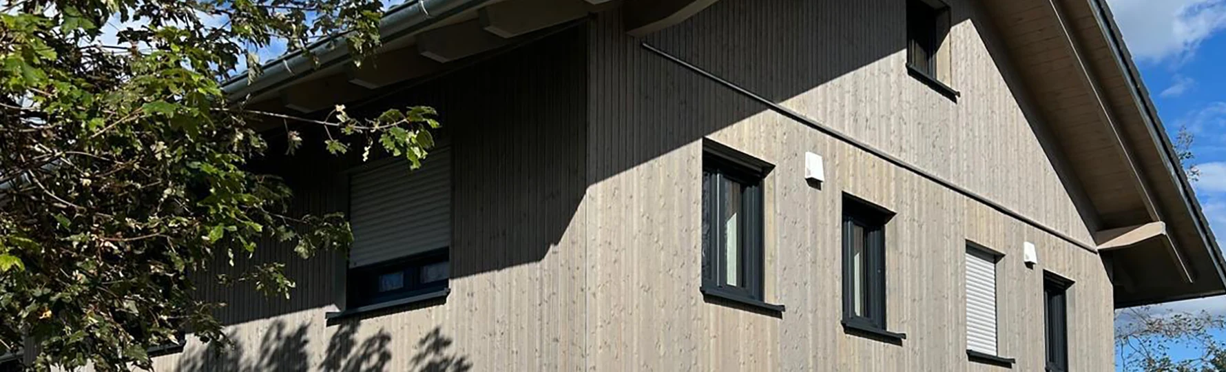 „Nahaufnahme eines Rohbaus mit rotem Ziegelmauerwerk, pinker Dämmschicht und sichtbaren Baugerüsten, mit der Aufschrift ‚Päuker Bau‘ über Fenstern.