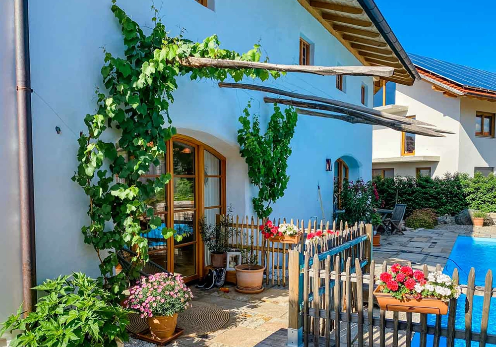 Blumenreicher Innenhof mit Holzzaun, Kletterpflanzen, Pool und Sitzbereich vor einem Haus mit Holzfenstern.