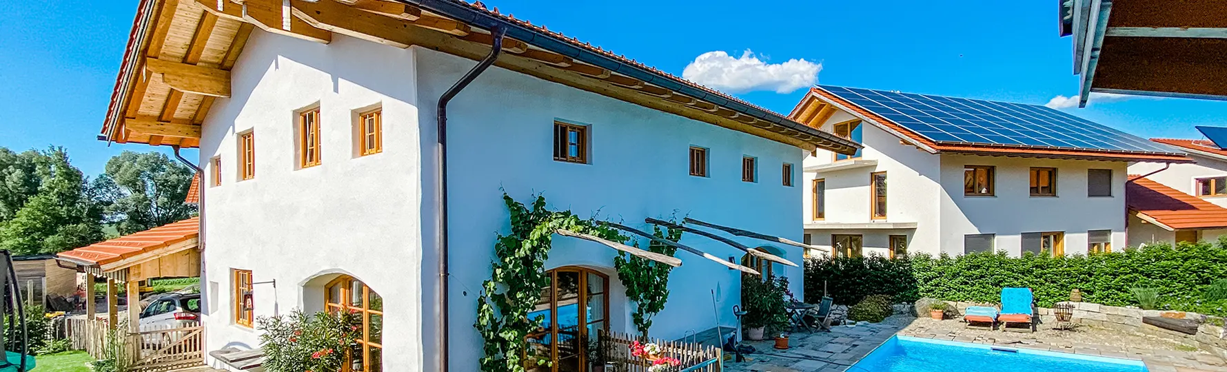 Innenhof mit weißem Haus, Kletterpflanzen, Pool und Sonnenliegen, daneben modernes Haus mit Solardach.