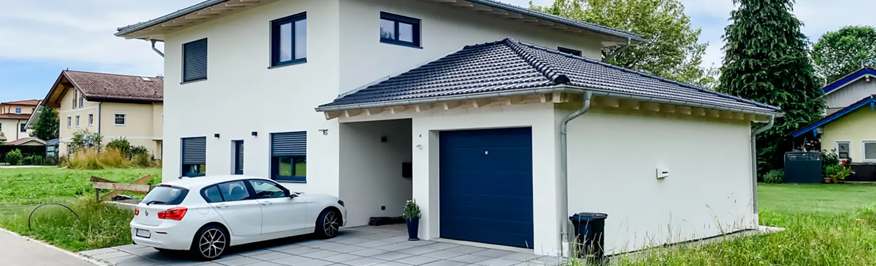 Modernes Einfamilienhaus mit Garage, blauen Fensterläden und weißem Auto in der Einfahrt.