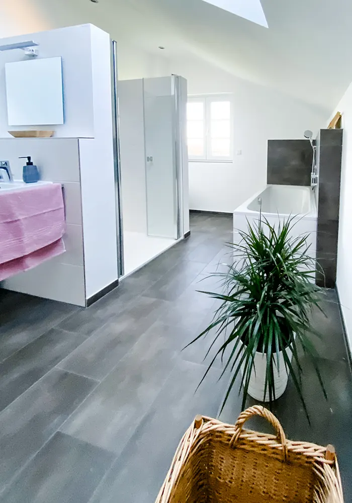 Modernes Bad mit grauem Fliesenboden, Badewanne, Dusche, Waschbecken und Zimmerpflanze in heller, heller Dachschräge.