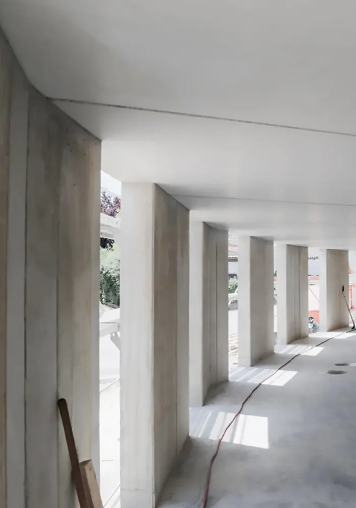 Innenansicht eines Rohbaus mit Betonstützen, glattem Boden und Licht von großen Öffnungen.