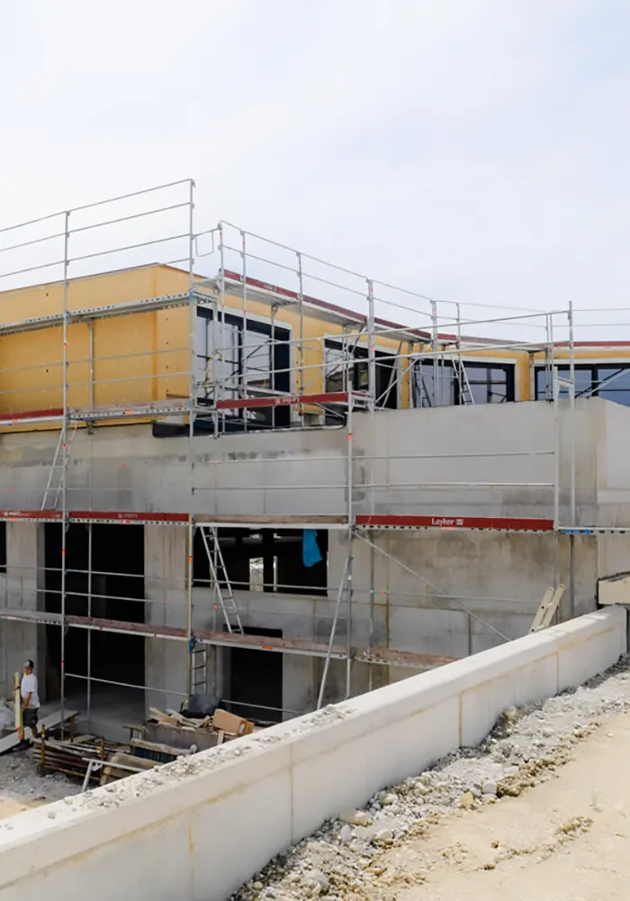 Zweistöckiger Rohbau mit Gerüsten und Bauarbeiter, Betonwände und große Fenster im oberen Stock.