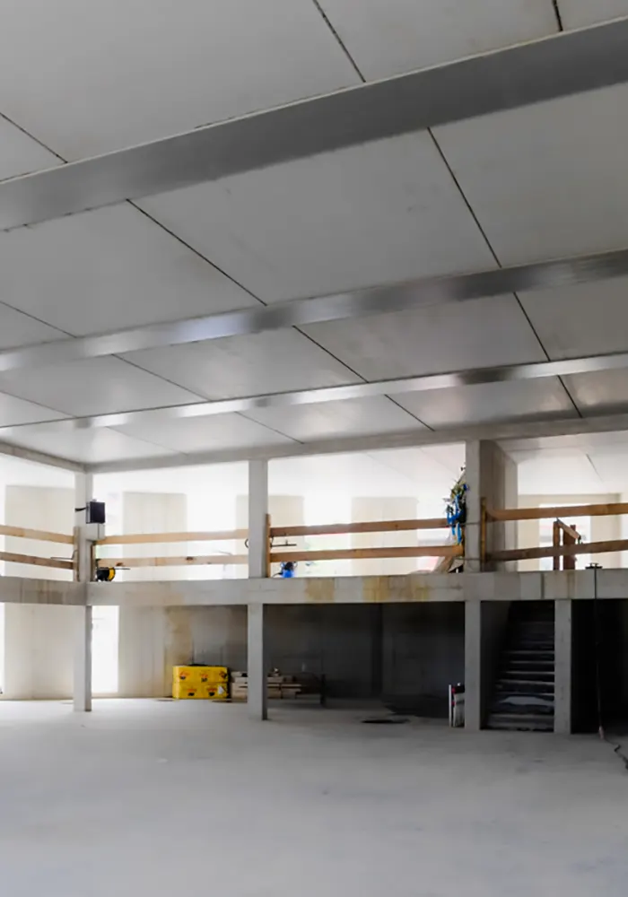 Innenaufnahme eines Rohbaus mit offener Galerie, Treppe und abgesicherten Geländern im Obergeschoss.