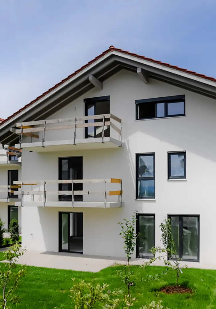 Mehrfamilienhaus mit weißer Fassade, Balkonen und gepflegtem Rasen im Vordergrund.