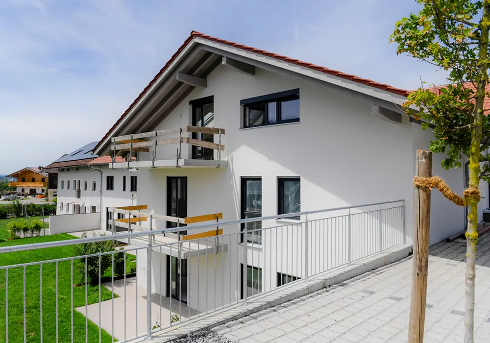 Neubau eines weißen Mehrfamilienhauses mit Balkonen, Vorgarten und gepflastertem Weg im Vordergrund.