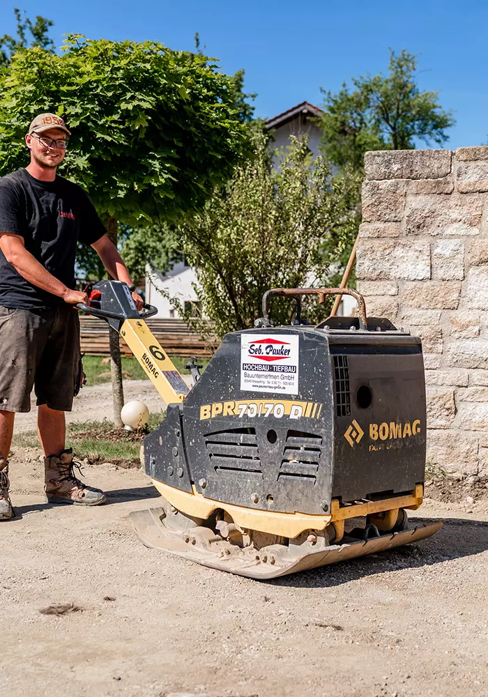 Bauarbeiter bedient eine Rüttelplatte zur Bodenverdichtung auf einer Baustelle.