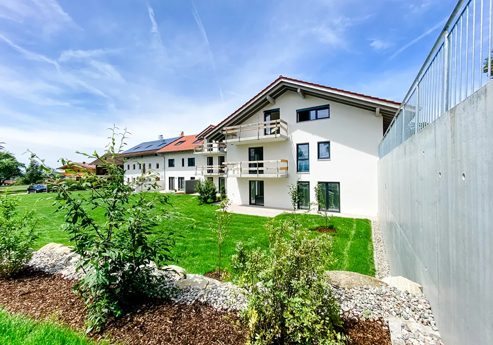 Mehrfamilienhaus mit Balkonen und gepflegtem Gartenbereich unter blauem Himmel mit Schleierwolken.