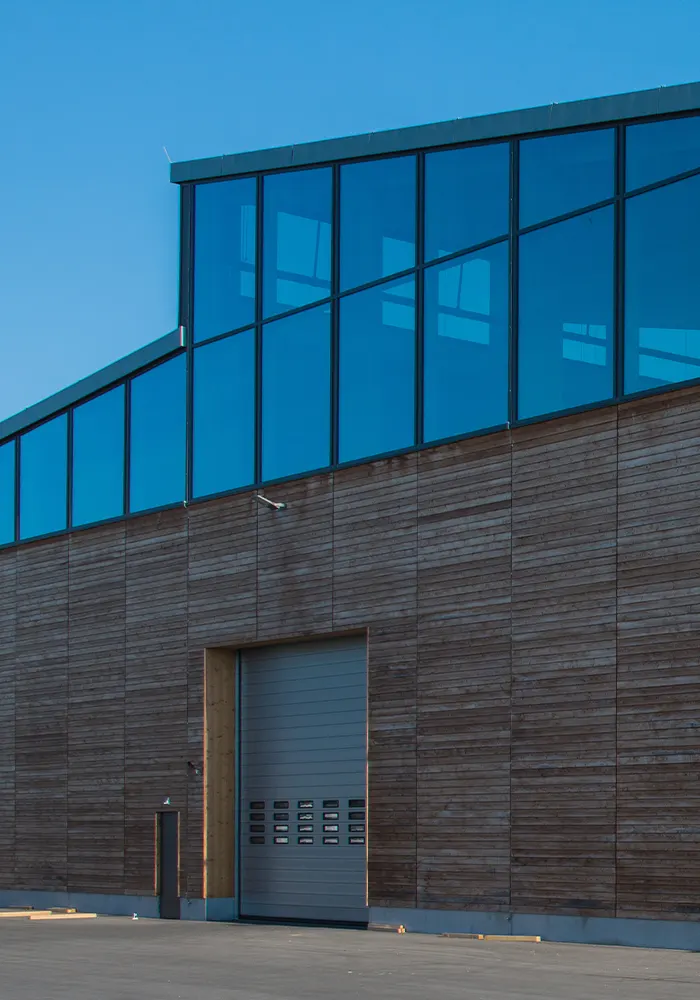 Moderne Halle mit Holzfassade und großer Glasfront, davor ein geschlossenes Rolltor.
