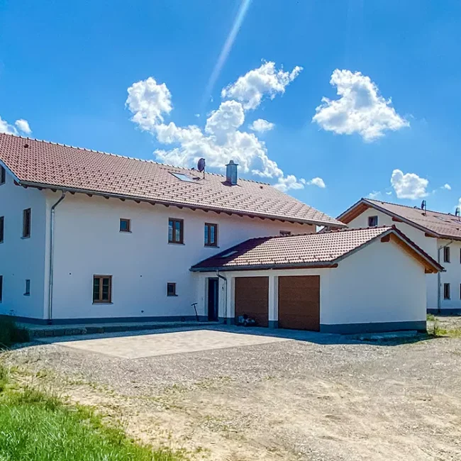 Zwei moderne Wohnhäuser mit rotem Satteldach, Garage im Vordergrund, unter blauem Himmel mit wenigen Wolken.